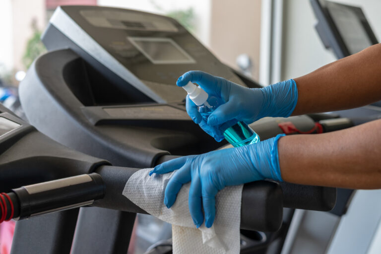 Staff using wet wipe and a blue sanitizer from the bottle to clean treadmill in gym. Antiseptic,disinfection ,cleanliness and healthcare, Anti Corona virus (COVID-19).